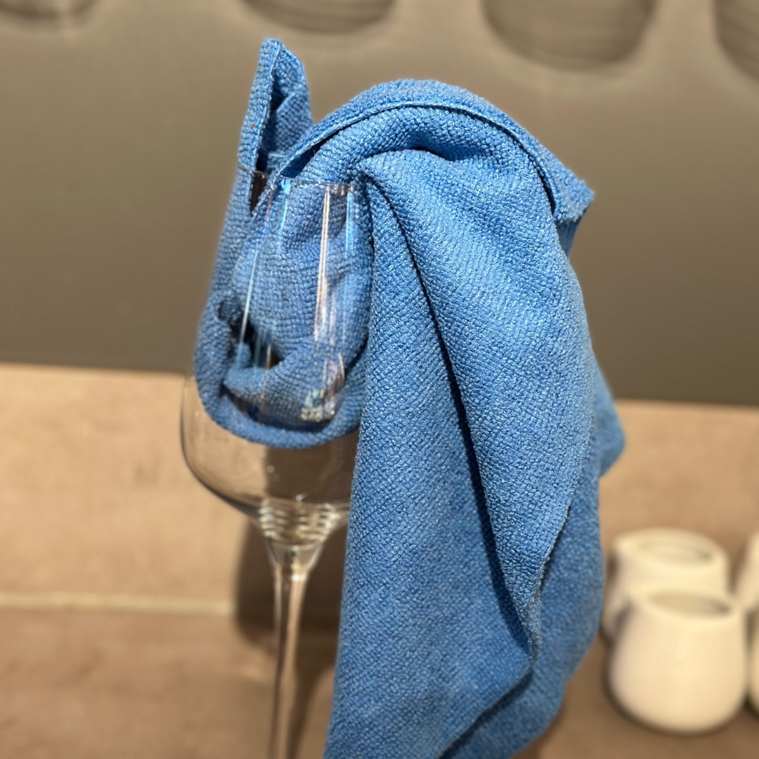 Blaues Mikrofasertuch in einem Trinkglas drapiert zur Demonstration der feinen Faserstruktur.