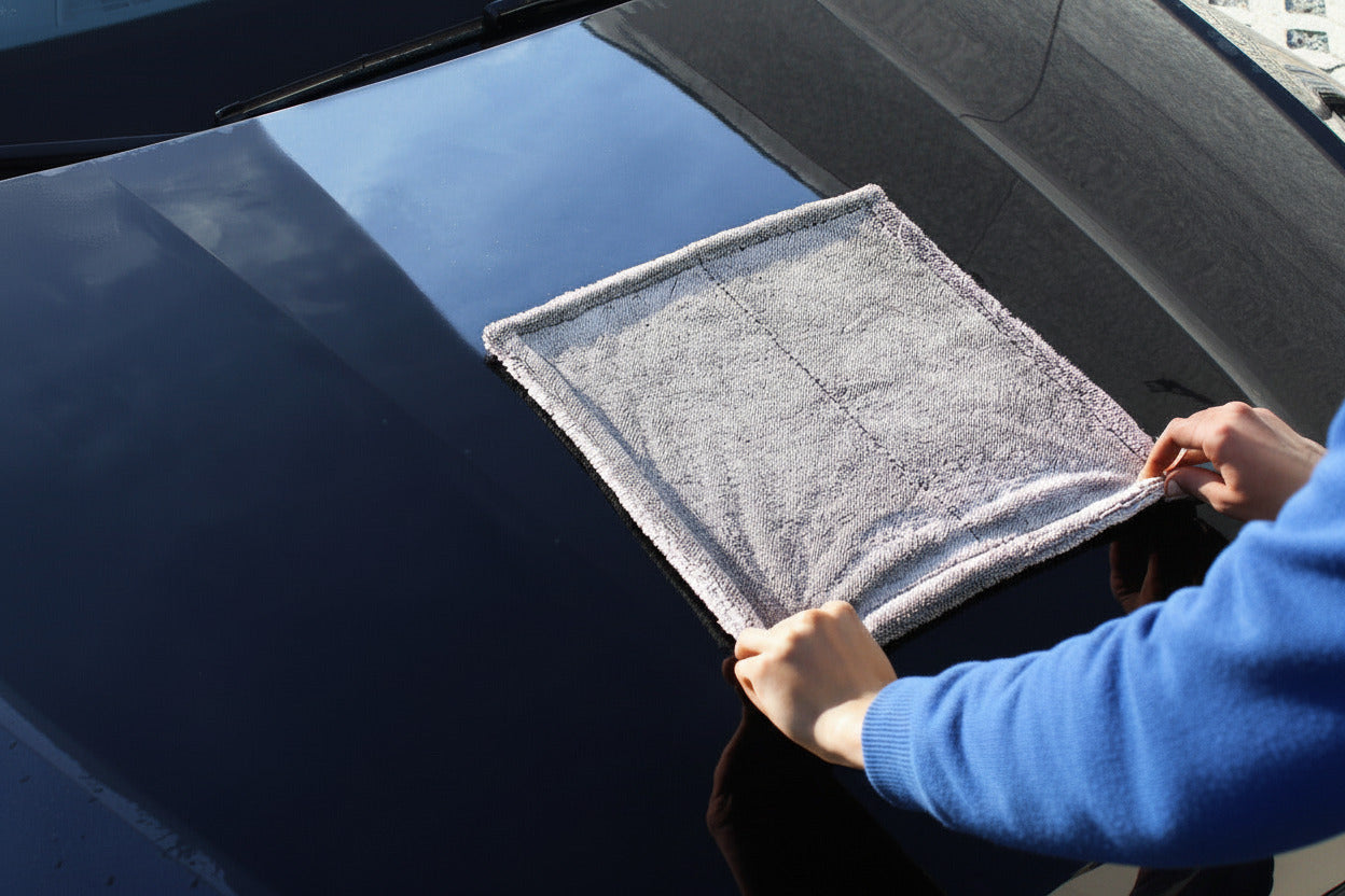 Blaues Mikrofasertuch Wassermagnet-Trockentuch im Einsatz auf einer dunklen Motorhaube zur streifenfreien Autotrocknung.
